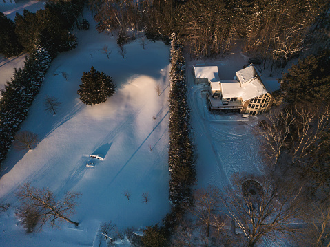 Sunrise view of Lake House in winter time. Large home in wooded area on the water edge of the lake. Georgian Bay area of Ontario province, Canada. Drone point of view.