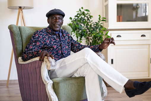 A smartly dressed Afro-Caribbean man is sitting in a comfortable armchair in a light bright room