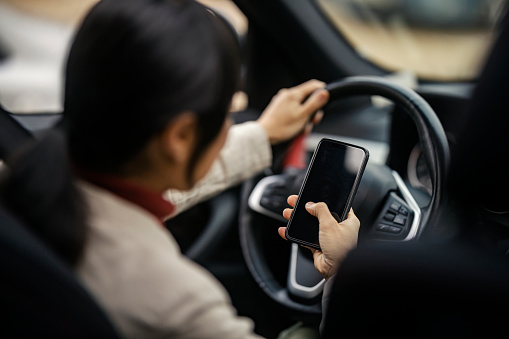 Back view of an asian woman driving a car and texting messages on the phone. Unsafe drive.