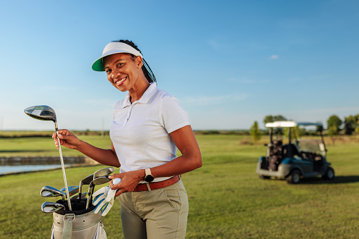 Female golf player smiling and posing while picking up a golf club on a field on a sunny summer day