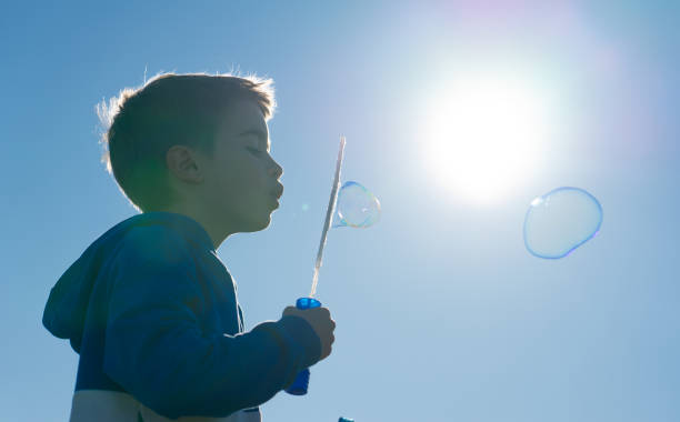 istock Boy blowing soap bubbles with the sun behind 1952608979