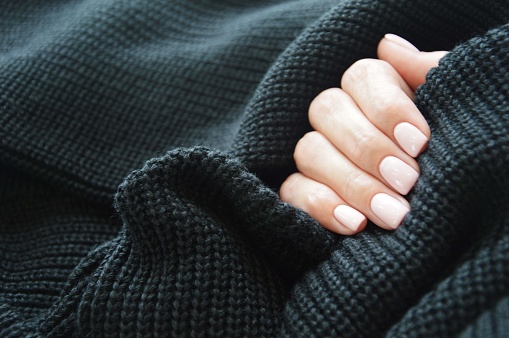 Female hands with a beautiful beige manicure in a warm black knitted sweater. Winter trend, gel polish, shellac.