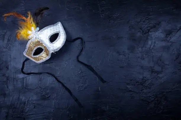Photo of White and gold mask with feathers, isolated on a textured black background