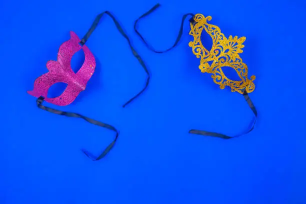 Photo of Two masks, one golden and the other violet, shiny and isolated on a blue background