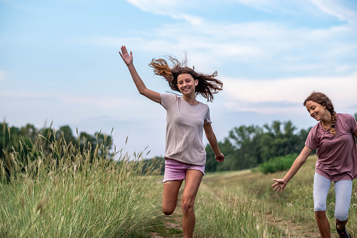 Two teenage girls are running by the forest and laughing.