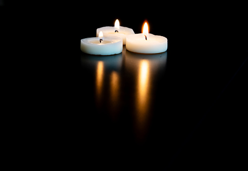three small candles grouped together lit on a table with a black background and empty space