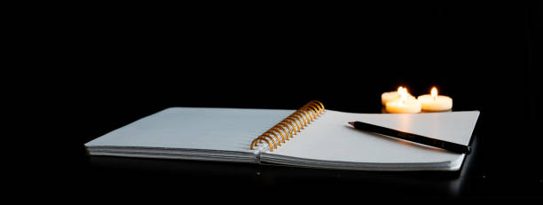 istock Open spiral notebook on a white page with a pencil on a black table with three small lit candles 1952656841