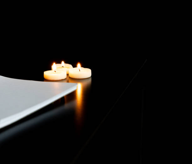 istock Open spiral notebook on a white page with a pencil on a black table with three small lit candles 1952657356