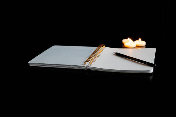 istock Open spiral notebook on a white page with a pencil on a black table with three small lit candles 1952657363