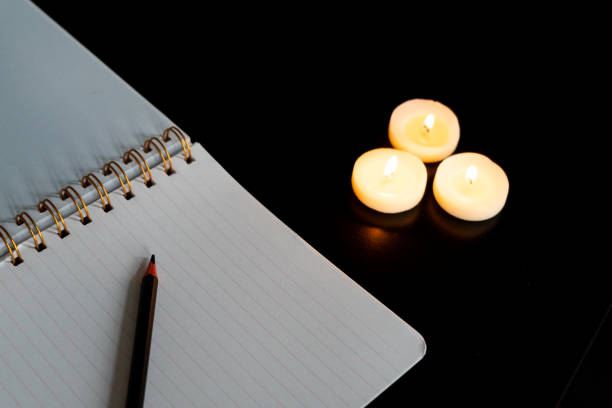 istock Open spiral notebook on a white page with a pencil on a black table with three small lit candles 1952658105