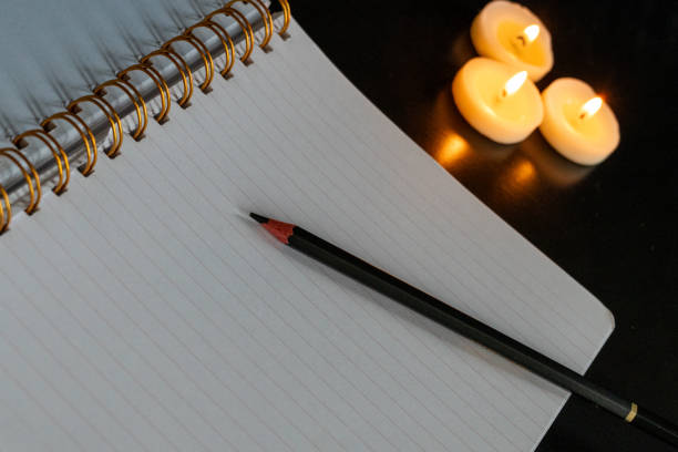 istock Open spiral notebook on a white page with a pencil on a black table with three small lit candles 1952658510