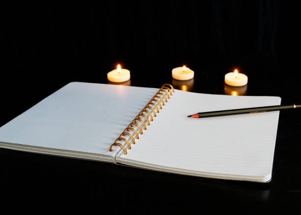 istock Open spiral notebook on a white page with a pencil on a black table with three small lit candles 1952659035