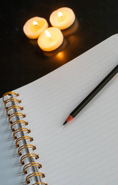 istock Open spiral notebook on a white page with a pencil on a black table with three small lit candles 1952659041