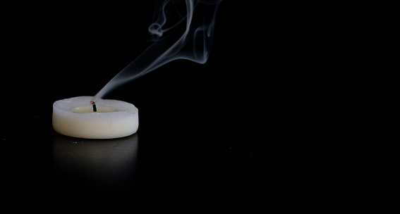 Extinguished candle with smoke on a black table with a black background and empty space