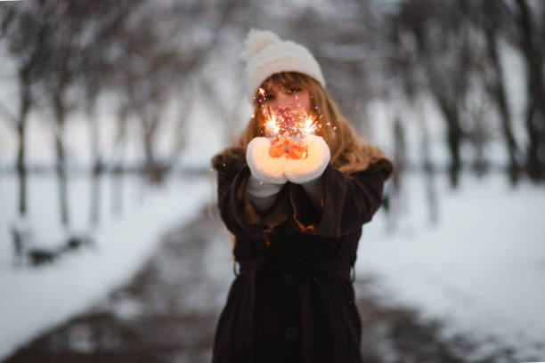Beautiful young woman holding sparklers while being in a public park. It is wintertime.
