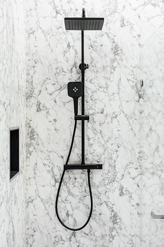 Black, modern designed shower head in a luxury bathroom covered with marble tiles
