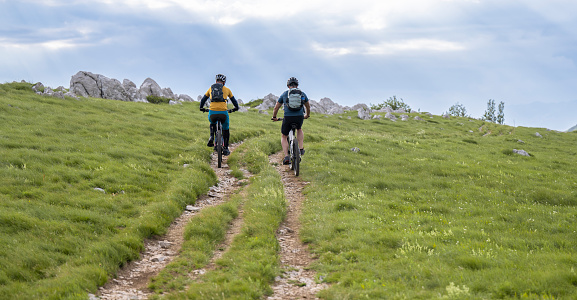 Two mid adult men wearing protective helmets riding electric mountain bikes together. Healthy lifestyle concept.