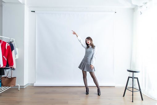 Asian woman in gray pleated skirt and white blouse pointing finger