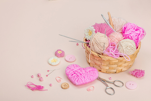 Handmade spring decor concept. Creative crocheting, traditional flowers and thread pink heart. Festive greeting card, gentle pastel apricot background, copy space