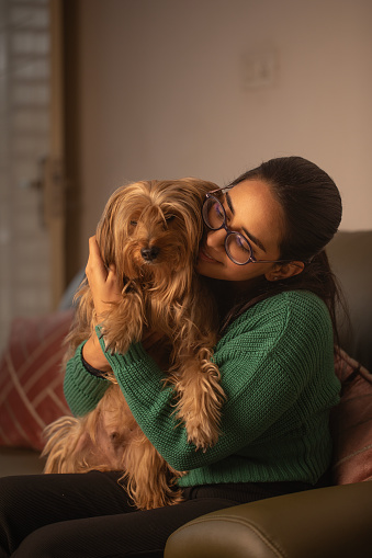 Happy loving young woman embracing furry Yorkshire Terrier while relaxing on sofa in living room at home