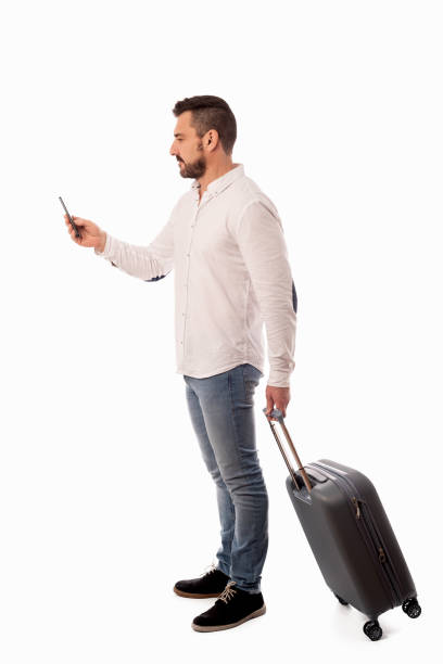istock Bearded man standing with a travel suitcase, looking at his cell phone on white background 1952749112