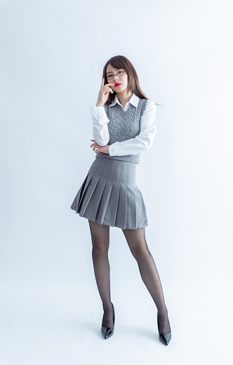 A young Asian woman in a gray pleated skirt and white blouse poses against a white background