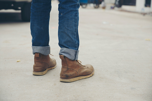 Legs of Lonely man wearing jeans and leather boots walking along the path strewn with rocks. Travel Concept.