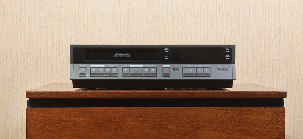 An old vintage VCR from the 1980s sits on the nightstand.