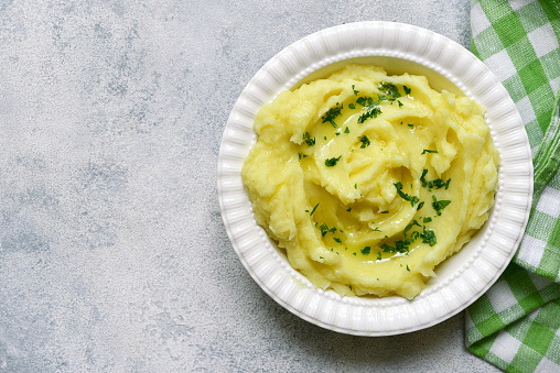Mashed potato in mediterranean style with rosemary, parmesan cheese, garlic and olive oil on a light slate, stone or concrete background. Top view with copy space.