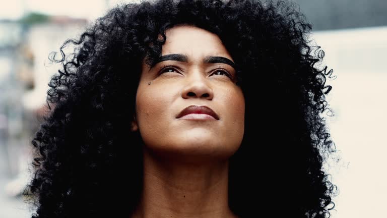 Young Spiritual African American woman looking up at sky BELIEVING and feeling the presence of a HIGHER POWER, belief and inspiration close-up face skyward