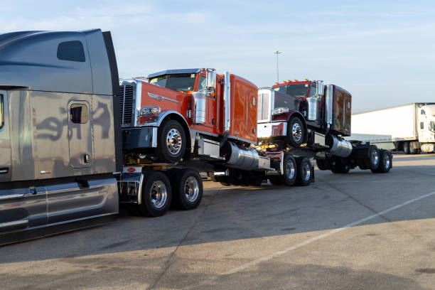 semi trucks parked in a row at truck stop during dusk. red semi truck towed on a trailer at truck stop - vehicle trailer flash photos et images de collection