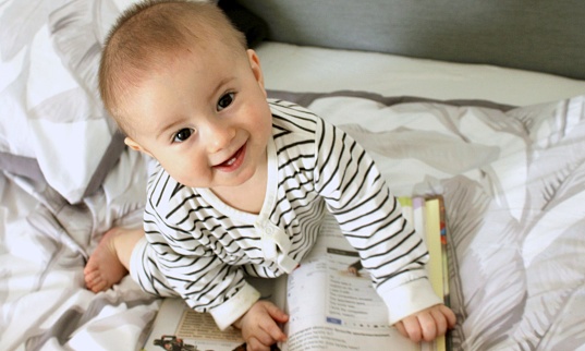 A cute little baby boy is carefully looking at a book with interest