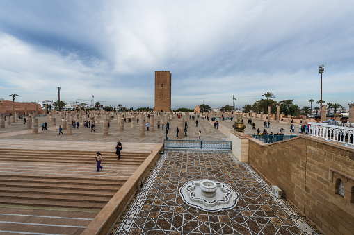 Rabat, Morocco - December 31, 2023: People in the square of the unfinished great mosque in Rabat. The 12th century Hassan Tower, also unfinished, is in the background.
