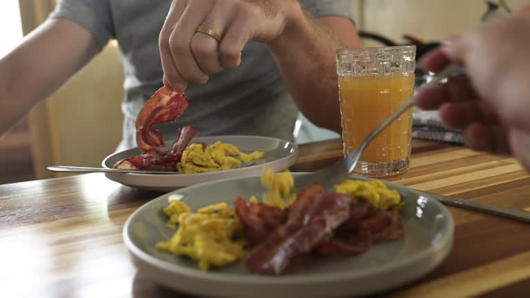 People, eating and breakfast of eggs or bacon, together and healthy food on kitchen counter in wellness. Couple, morning and scramble with pov and protein meal for nutrition for weekend in apartment