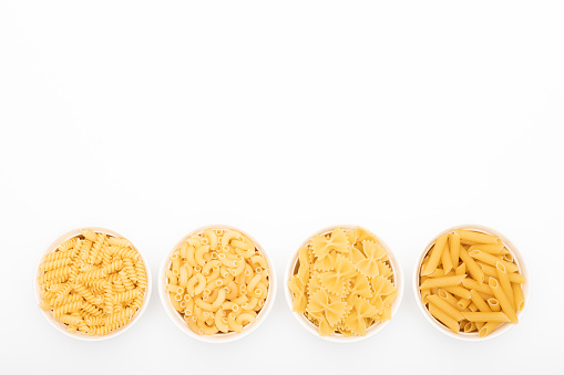 Different types of pasta in small bowls on a white background