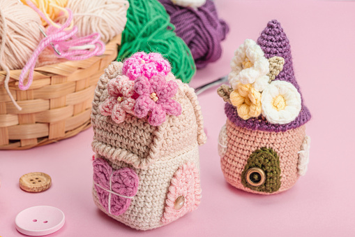 Handmade spring decor concept. Creative crocheting, house figurines, traditional flowers and stuff. Festive greeting card, gentle pastel pink background, close up