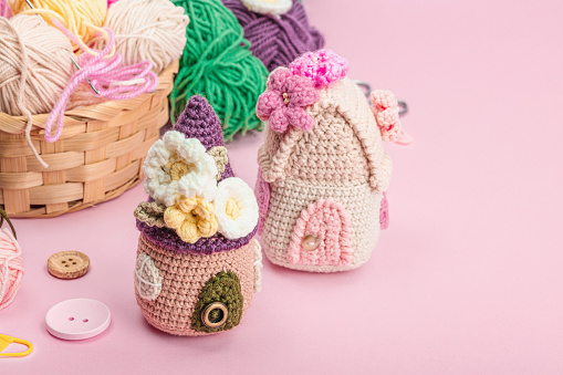 Handmade spring decor concept. Creative crocheting, house figurines, traditional flowers and stuff. Festive greeting card, gentle pastel pink background, copy space