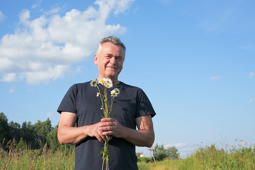 Romantic smiling senior man with flowers, bouquet of chamomiles in man's hands. High quality photo
