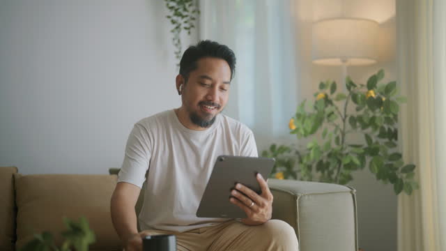 Handsome young Latino man using a digital tablet He is working from home in his living room.