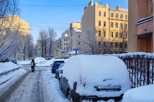 St. Petersburg, Russia - January 21, 2024: People and parked cars on a snowy street in the center of the old city on a clear sunny day. Winter cityscapes