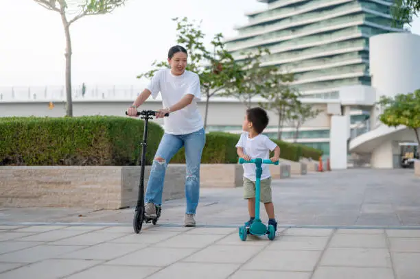 Experience the pure delight as a vibrant, multiracial two and a half year old boy joyfully rides a scooter with his loving, smiling Chinese mom. The shared moments of laughter and exploration create cherished memories
