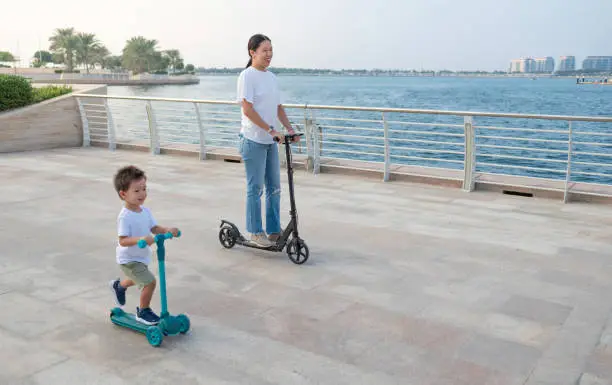 Delight in the seaside breeze as a charming two and a half year old multiracial boy and his Chinese mother enjoy a carefree scooter ride along the scenic promenade. A heartwarming blend of cultural diversity and mother-son joy against the backdrop of the serene sea