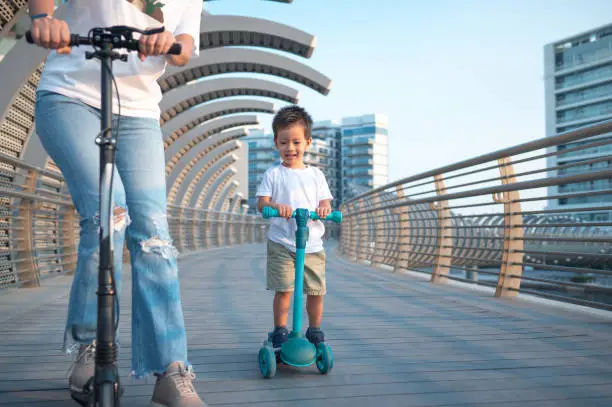 Experience the pure delight as a vibrant, multiracial two and a half year old boy joyfully rides a scooter with his loving mom. The shared moments of laughter and exploration create cherished memories