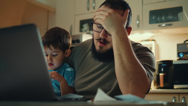 Single father is annoyed reading bills, paying bill invoices with increased price budget expenses. Unset man with a little son looking at his financial debts