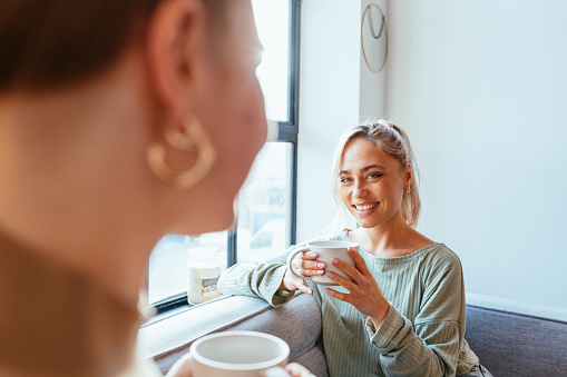 Two best female friends drinking coffee and talking at home