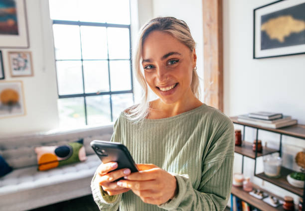 istock Millennial woman using smart phone at home. Blonde woman using mobile app on mobile device 1952960255