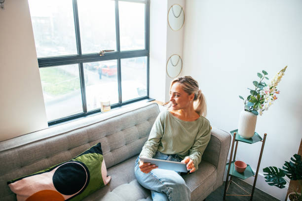 istock Young beautiful woman at home using digital tablet and looking through the window 1952960801