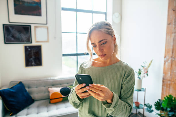 istock Millennial woman using smart phone at home. Blonde woman using mobile app on mobile device with serious expression 1952960805