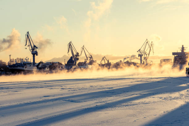 Tower cranes in misty background, deep sunset shadows on the snowy frozen river