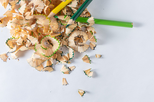 Top view photo of green and yellow colored pencils with shavings on a white background.